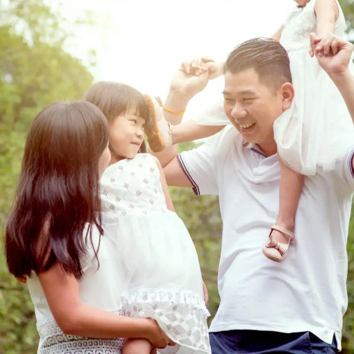 Family of four outdoors with a woman holding a child and a man carrying another child.